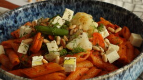 Eine blaue Schale gefüllt mit FRoSTA Penne all’Arrabbiata, Tomatensauce, Käsewürfeln, geröstetem FRoSTA-Gemüse, Pinienkernen und frischen Kräutern.