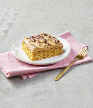 Ein FRoSTA-Tiefkühlkuchen mit Espresso-Glasur und Schokodrizzle liegt auf einem weißen Teller neben einer goldenen Gabel.