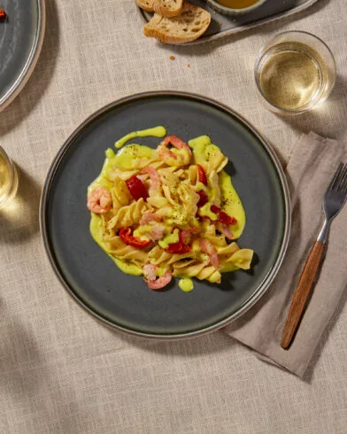 Pasta al Limone mit FRoSTA Garnelen und roter Paprika in cremiger Sauce auf grauem Teller, dazu Wein und Brot.