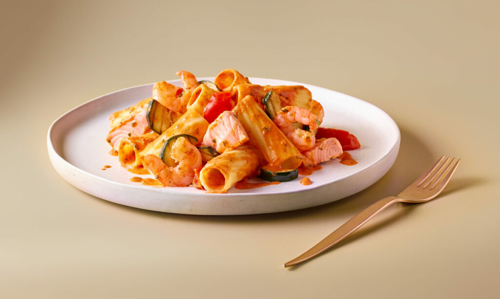 Rigatoni mit FRoSTA-Garnelen, Tomaten und Basilikum in cremiger Sauce auf weißem Teller-Restaurantgenuss ohne Reservierung.