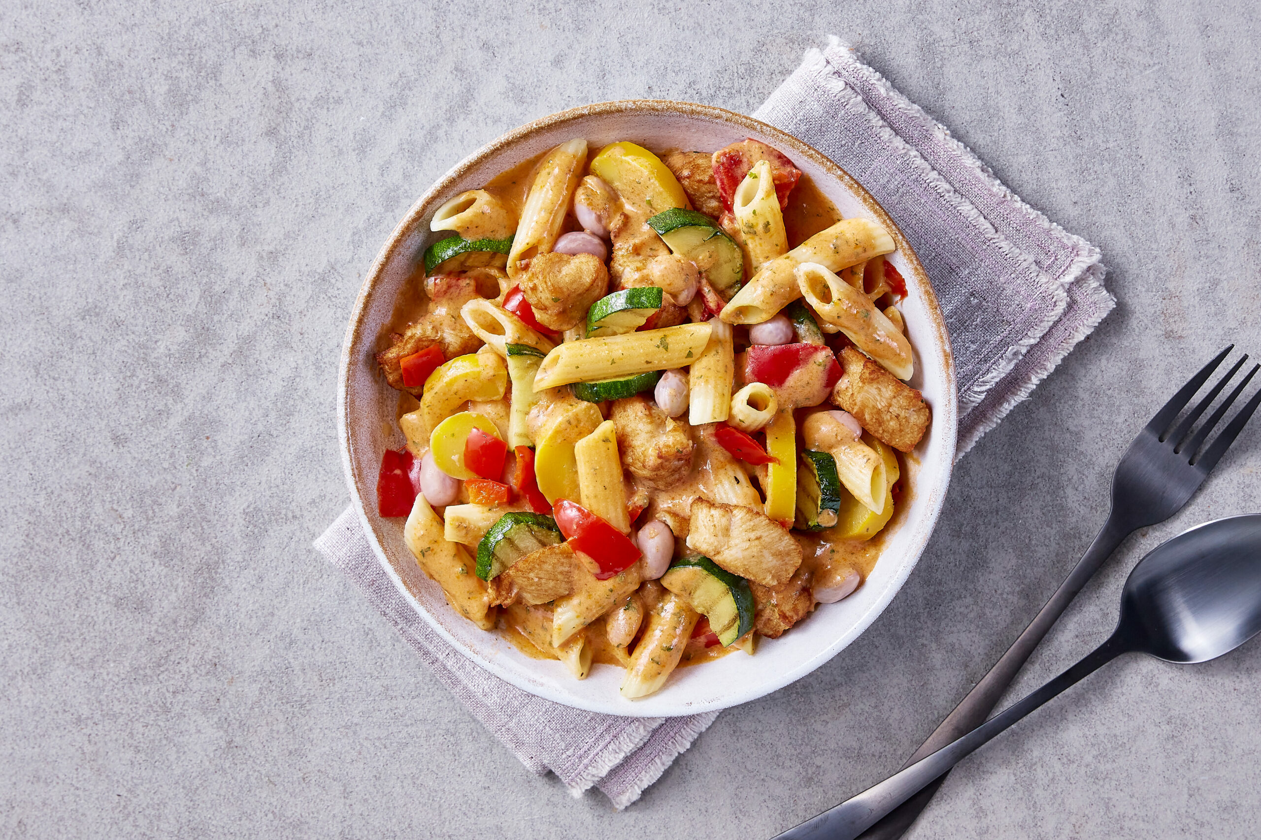 Cremige Penne mit FRoSTA-Hähnchen, Zucchini, Paprika und gelbem FRoSTA-Kürbis auf einem rustikalen Teller, von oben fotografiert.
